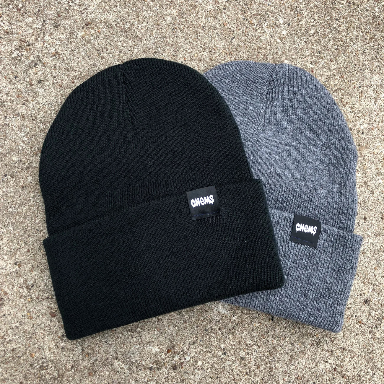 Black and Gray Chems Beanie Hats; Features a black tag with white "CHEMS" text; Stylish and versatile accessory for keeping warm;