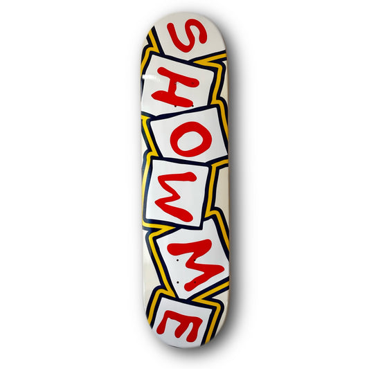 Show Me Blocks Skateboard Deck; skateboard deck features illustrated graphic of white blocks outlined in yellow and black; Red letters on the blocks spell out “Show Me”; background is off-white